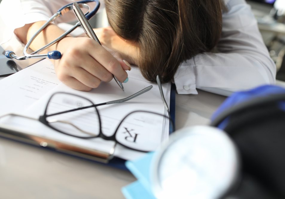 Close-up of exhausted medical worker laying on working table writing prescription. Long day at clinic. Tired female fell asleep on desk at work. Medicine concept