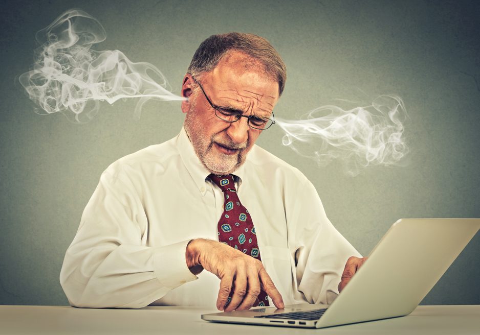 Stressed old man using computer blowing steam from ears Confused looking elderly mature man with glasses sitting at table working typing on laptop computer